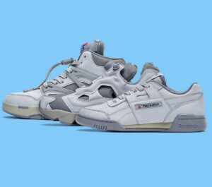 Reebok x PlayStation collab shoes displayed side by side on a medium sky blue background, featuring grey tones with subtle PlayStation branding and a mix of classic and futuristic design elements.