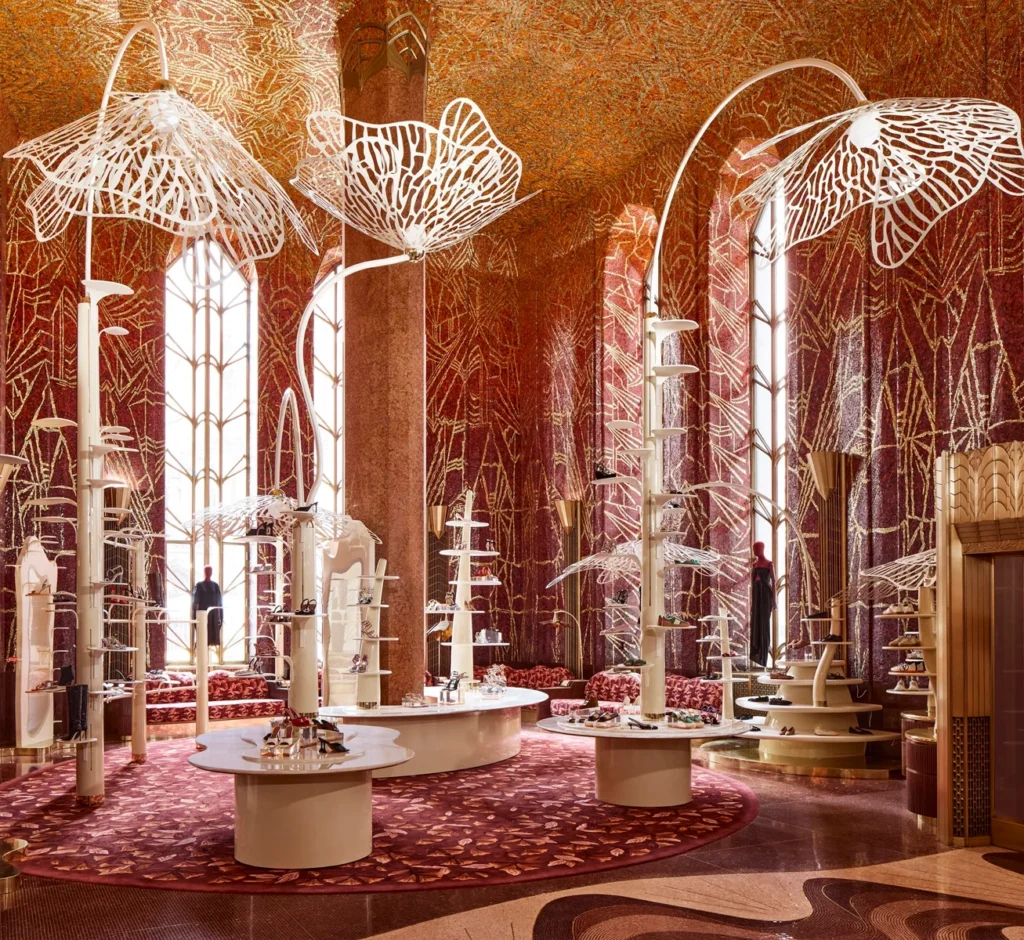 Interior of Printemps Haussmann in Paris featuring ornate Art Deco architecture with tall arched windows, gold and red patterned walls, and sculptural white display structures resembling abstract flowers under a mosaic ceiling.