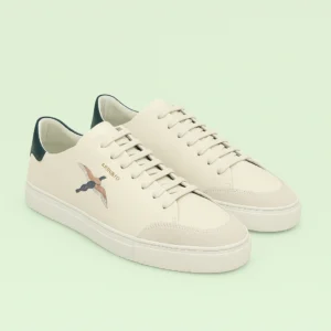 Axel Arigato Clean 90 Bee Bird sneakers in off-white leather with multicolour embroidered bird motif and dark green heel tab, photographed on a light green background, showcasing their minimalist Scandinavian design and premium craftsmanship.