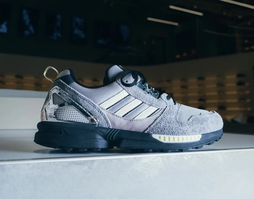 Side profile of the Offspring x mita x adidas ZX 8000 sneaker in grey suede and mesh with chrome heel clip and black sole, photographed under store lighting — symbolizing the ‘14,000 kilometre-wide dap’ connection between London and Tokyo.
