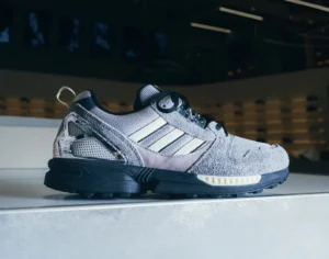 Side profile of the Offspring x mita x adidas ZX 8000 sneaker in grey suede and mesh with chrome heel clip and black sole, photographed under store lighting — symbolizing the ‘14,000 kilometre-wide dap’ connection between London and Tokyo.