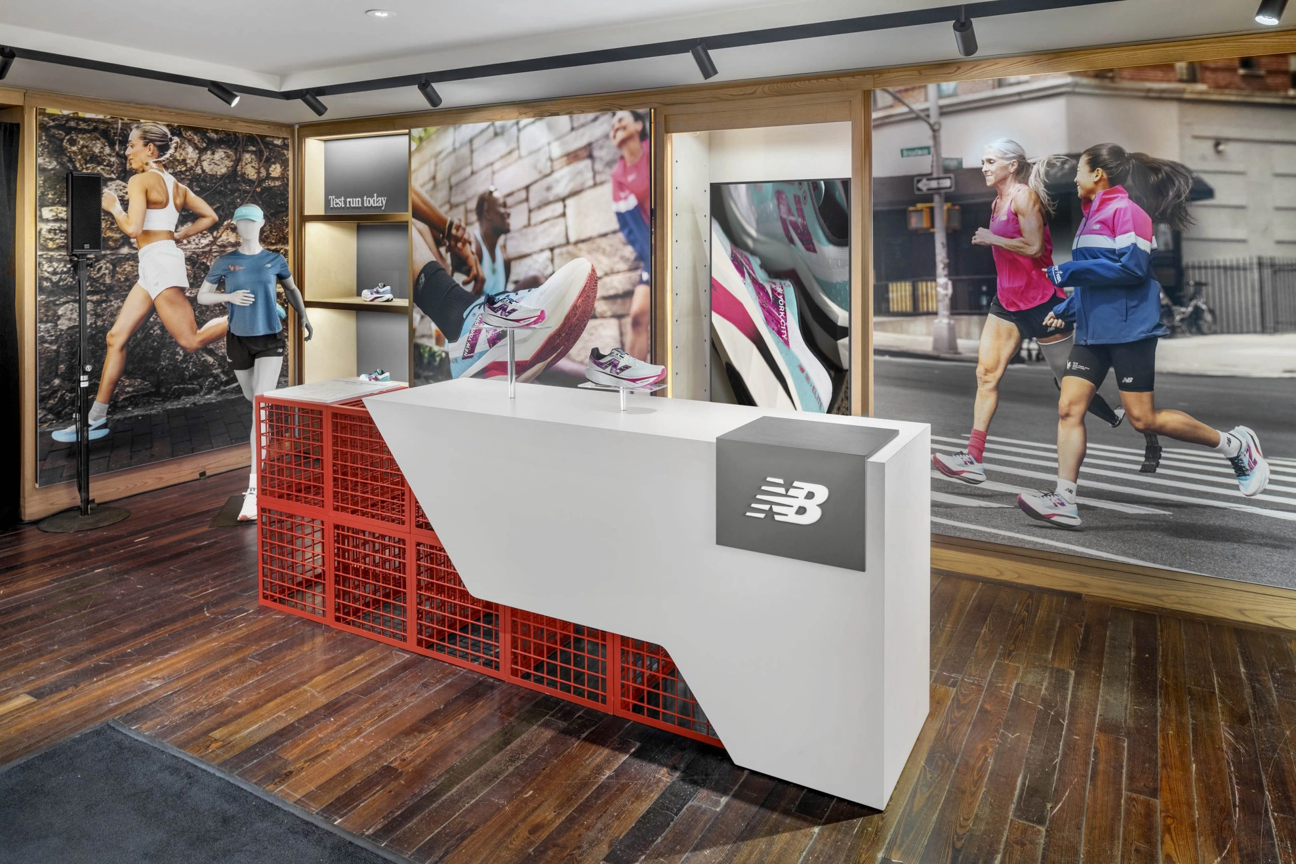 Interior view of a New Balance retail space featuring marathon-themed displays, including mannequins dressed in running gear, vibrant wall murals of athletes in motion, and a white counter with red lattice detailing showcasing the latest FuelCell running shoes on wooden flooring.