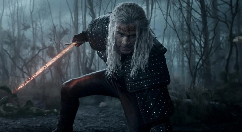 Geralt of Rivia, dressed in dark studded armor, crouches in a misty forest with a bloodied face and glowing steel sword drawn, ready for battle in a tense scene from The Witcher.