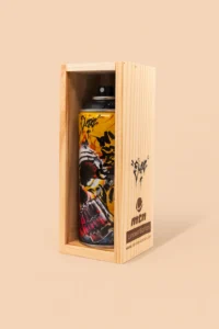 A limited edition Montana Colors spray paint can designed by Chaz Bojórquez, displayed in a light wooden box. The can features vivid graffiti artwork of a skull in red, yellow, and black tones, with Bojórquez’s signature tags visible near the top. Set against a soft beige-pink background, the image highlights the collectible’s craftsmanship and street-art heritage.