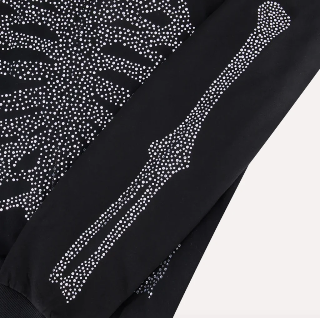 Close-up of the Rolling Loud WEATSHIRT RL Bones Zip Up Hoodie sleeve, showing a rhinestone-embellished arm bone graphic aligned with the ribcage design on black cotton fabric.