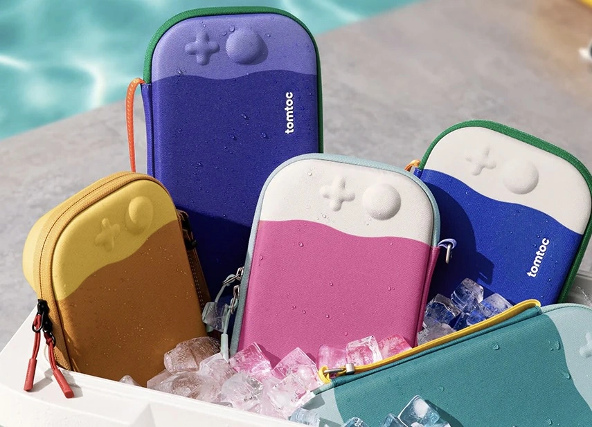 A collection of colorful Tomtoc Switch 2 carrying cases arranged beside a pool, resting on ice. Each case features a skittish two-tone design with embossed control buttons, shown in shades of blue, pink, green, yellow, and purple, highlighting their summer-ready, water-resistant style.