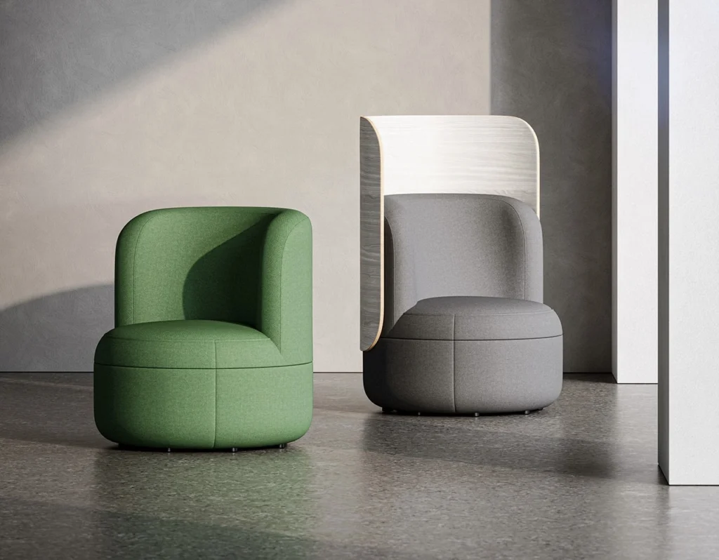 Two lounge chairs from KFI Studios’ Dotti Collection are placed in a softly lit, minimalist interior. The chair on the left is upholstered in green fabric with a low, rounded back, while the chair on the right features gray upholstery and a tall, curved wooden back panel in a light ash tone. The clean geometry and natural light emphasize the collection’s balance between comfort, craftsmanship, and modern elegance.
