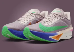 Close-up of the Nike Zoom Fly “No Human Is Limited” running shoes inspired by Eliud Kipchoge. The design features a beige mesh upper with a vivid green Swoosh, bright blue midsole, neon green outsole, and orange heel accent. The words “No Human Is Limited” are printed near the heel, symbolizing Kipchoge’s personal mantra. The shoes are displayed on a muted mauve background, emphasizing their vibrant contrast and aerodynamic shape.