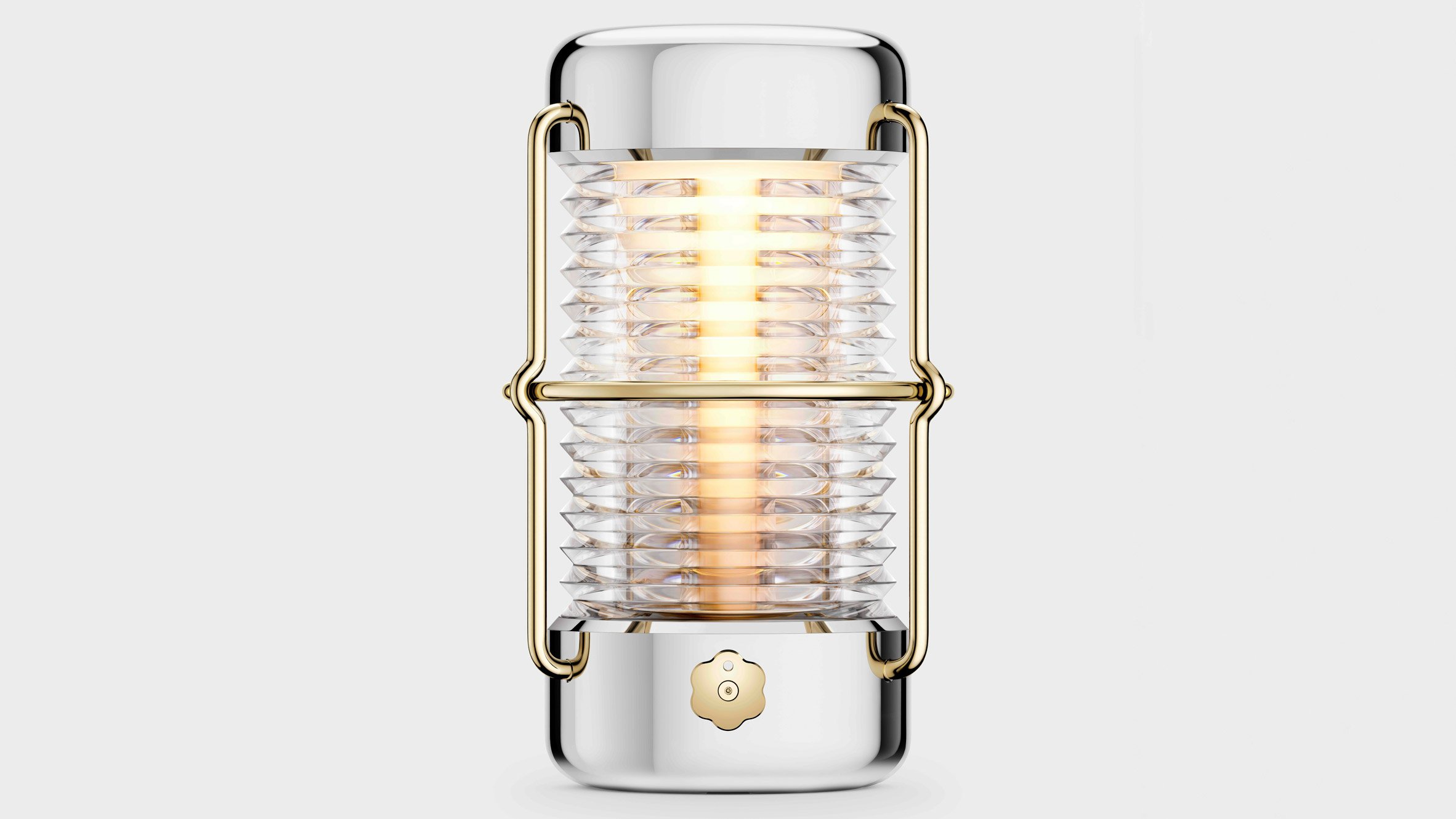 Front view of the Balmuda “Sailing Lantern” designed by Jony Ive, featuring a ribbed glass cylinder encased in polished aluminum and gold-toned brass, emitting a warm ambient glow.