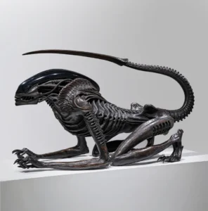 Life-size Necronom sculpture by H.R. Giger, created for Alien III, depicting a crouched biomechanical creature with an elongated, ridged tail and glossy black exoskeletal head, blending anatomical and mechanical details; displayed on a white plinth at Mai 36 Galerie during H.R. Giger Paris exhibition, 2025.