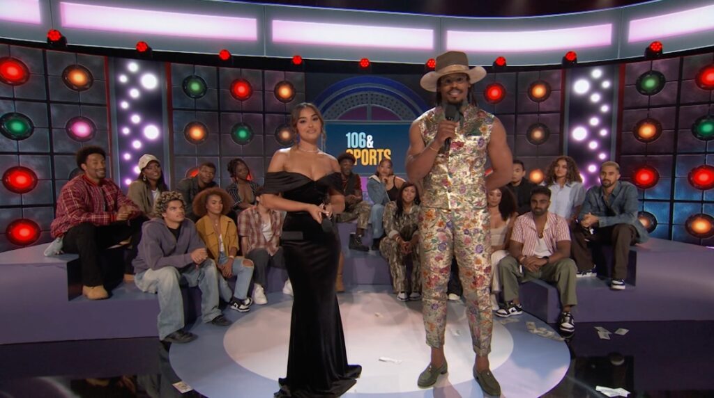 Cam Newton and Ashley Nicole Moss host BET’s 106 & Sports on stage in front of a live studio audience, with colorful light panels and the show’s logo in the background.