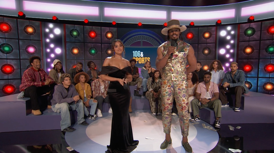 Cam Newton and Ashley Nicole Moss host BET’s 106 & Sports on stage in front of a live studio audience, with colorful light panels and the show’s logo in the background.