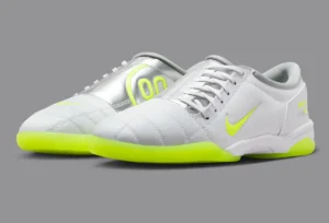Pair of Palace x Nike Total 90 III sneakers featuring a white leather upper with metallic silver panels, Volt green Swoosh accents, and bright neon outsoles, shown on a neutral gray background highlighting their sleek, retro-futuristic Y2K design.