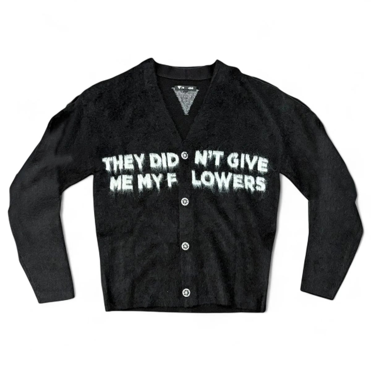 Black fuzzy-textured VALABASAS cardigan with distressed white text reading “THEY DIDN’T GIVE ME MY FLOWERS” across the chest
