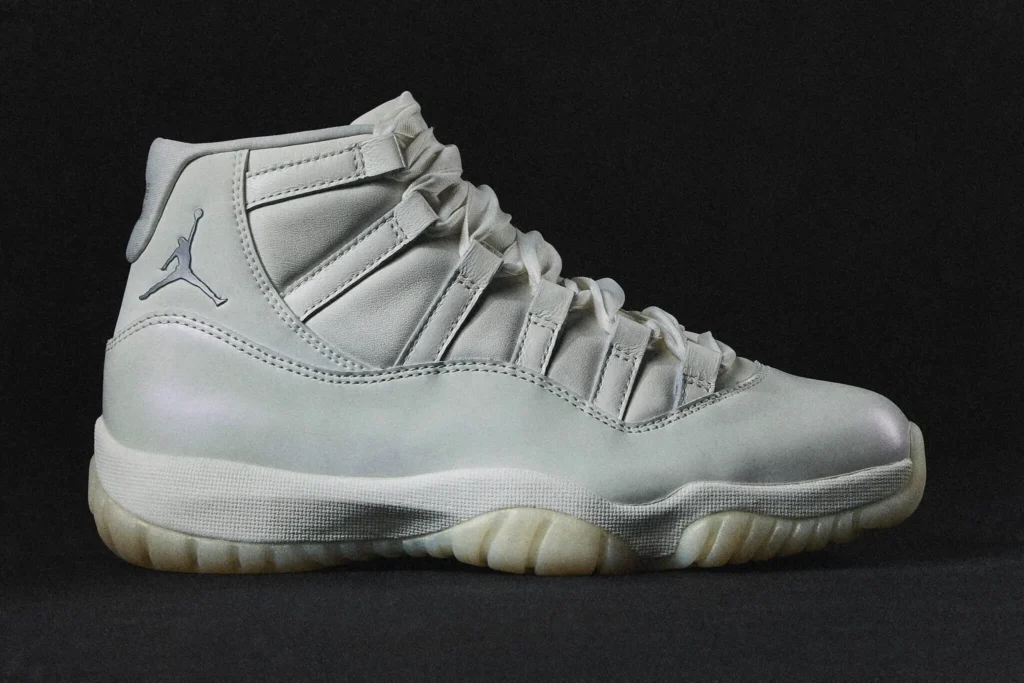 Air Jordan 11 WMNS “Pearl” sneaker shown in a side profile against a dark background, featuring a soft champagne-toned upper, pearlescent patent detailing, and a milky translucent outsole