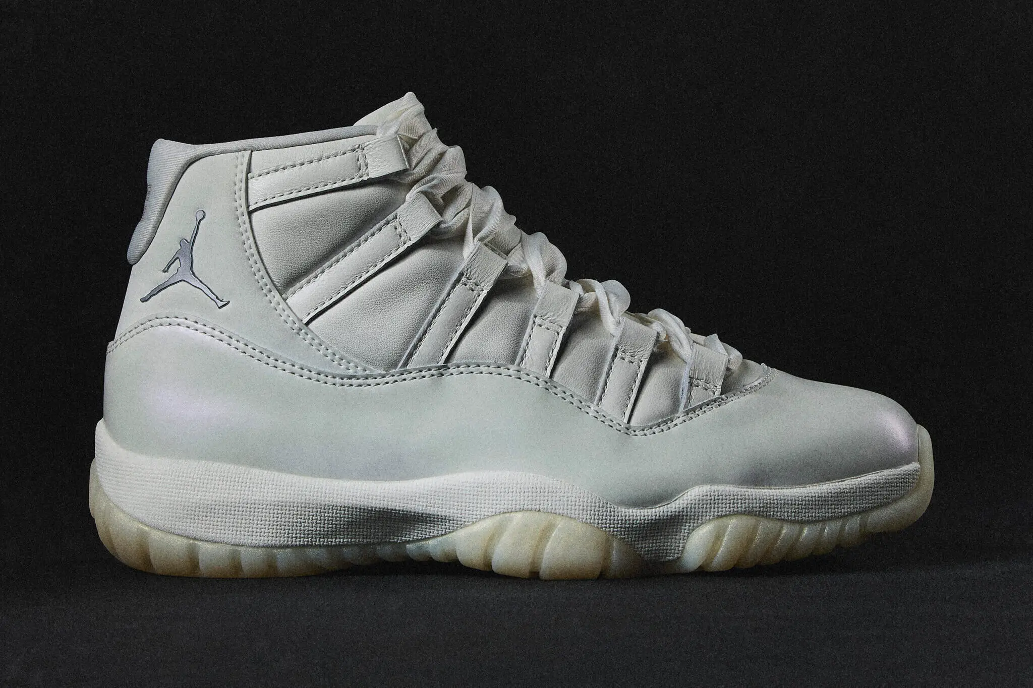 Air Jordan 11 WMNS “Pearl” sneaker shown in a side profile against a dark background, featuring a soft champagne-toned upper, pearlescent patent detailing, and a milky translucent outsole