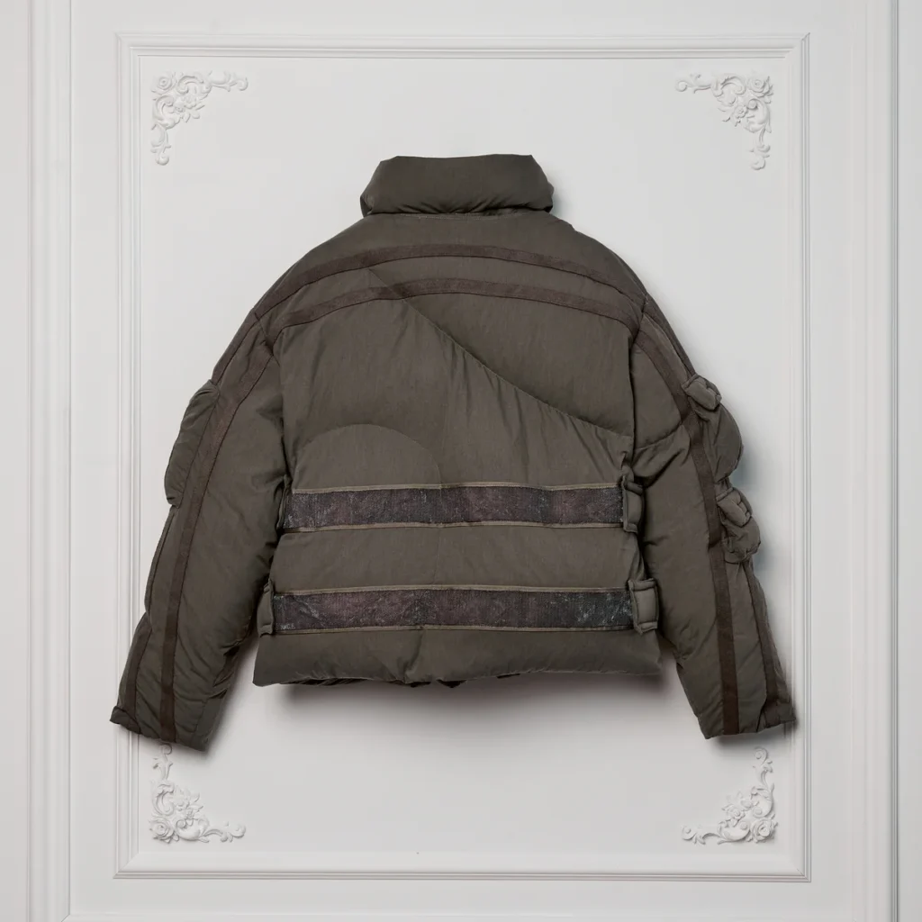 Back view of the Kody Phillips Cargo Puffer in Sage featuring quilted panel construction, wide horizontal webbing reinforcements, and articulated sleeve detailing for a structured utilitarian look