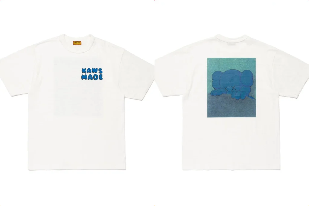 Front and back view of a white HUMAN MADE × KAWS “KAWS MADE” T-shirt. The front features the “KAWS MADE” logo in blue bubble letters, while the back displays KAWS’ blue Companion artwork resting its head on folded arms against a soft gradient background, combining artful melancholy with streetwear precision