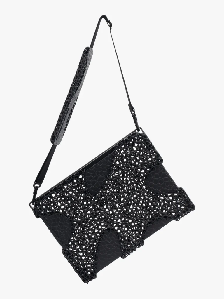 close-up of the virga laptop sleeve from the aliveform × côte&ciel “living systems” capsule, featuring a black 3d-printed lattice shell with organic cellular geometry layered over a matte base, suspended by a detachable strap with matching perforated detailing