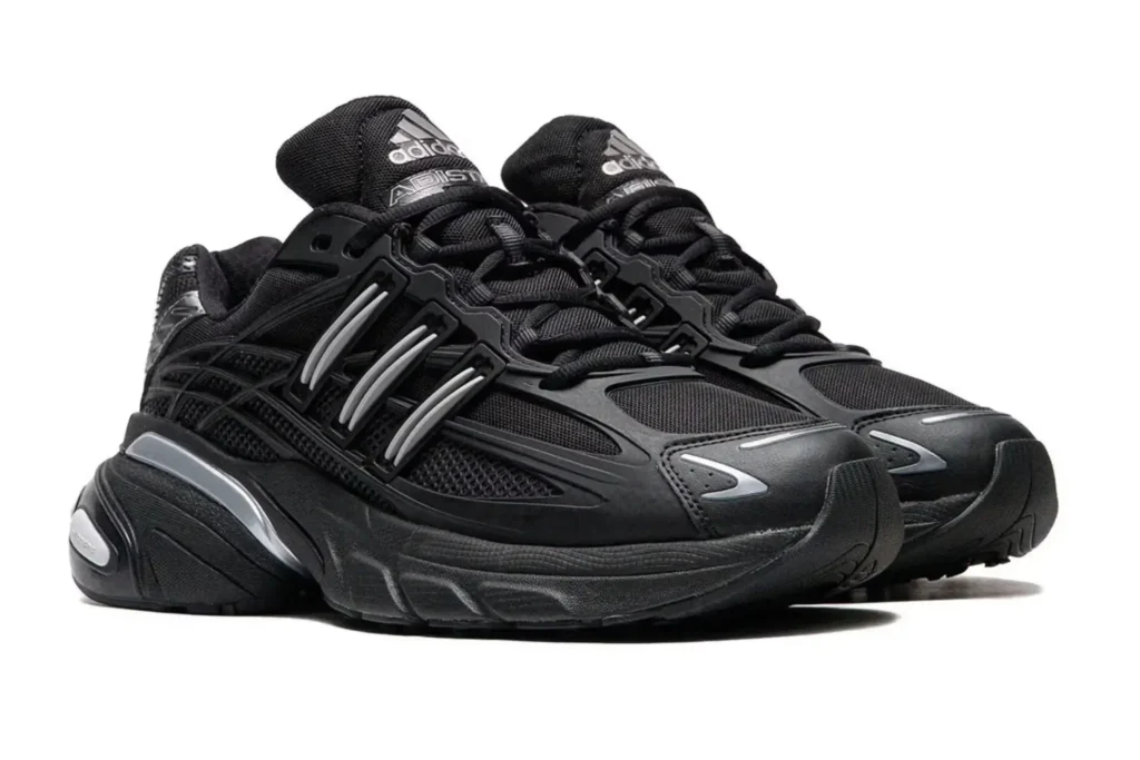 A pair of adidas Adistar XLG 2.0 sneakers in an all-black colorway, featuring layered mesh and synthetic overlays, glossy black structural cages, silver reflective accents, and a chunky sculpted midsole, photographed against a white background