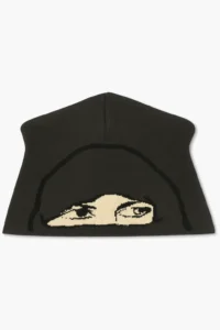 Black knit skully beanie displayed on a white background, featuring a beige woven graphic of a hooded figure’s eyes across the front