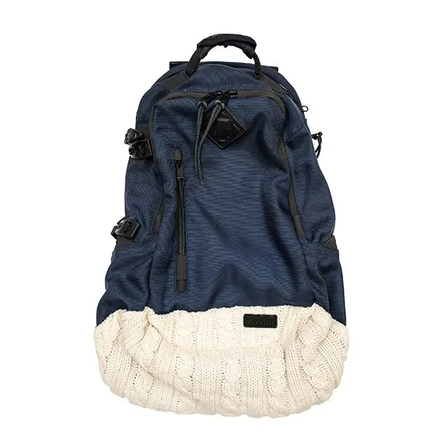 A visvim backpack featuring a navy technical fabric upper and a contrasting cream cable-knit bottom panel, blending outdoor utility with artisanal textile detailing