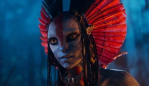 A Na’vi character from Avatar: Fire and Ash with blue skin, yellow eyes, and braided hair, wearing a striking red feathered headdress against a glowing blue jungle background.