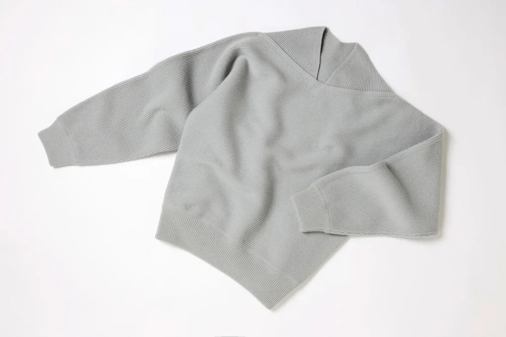 Flat-lay of the recreated Brutalist Sweater in soft grey, showing its wide ribbed knit texture, relaxed silhouette, and asymmetric neckline against a clean white background