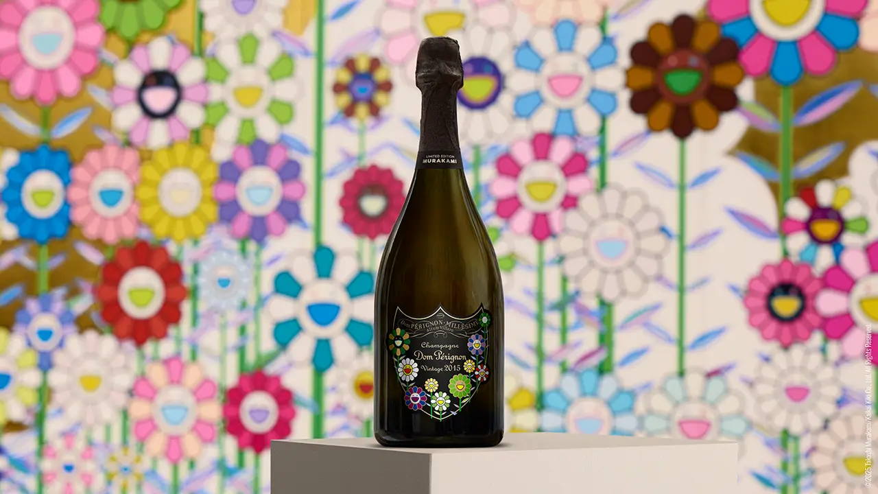 A limited-edition Dom Pérignon Vintage 2015 champagne bottle designed by Takashi Murakami stands on a pedestal against a vivid backdrop of Murakami’s iconic smiling flowers. The bottle’s classic dark green form features Murakami’s colorful floral motifs integrated into the Dom Pérignon shield label, symbolizing the fusion of fine champagne craftsmanship with contemporary Japanese pop art.
