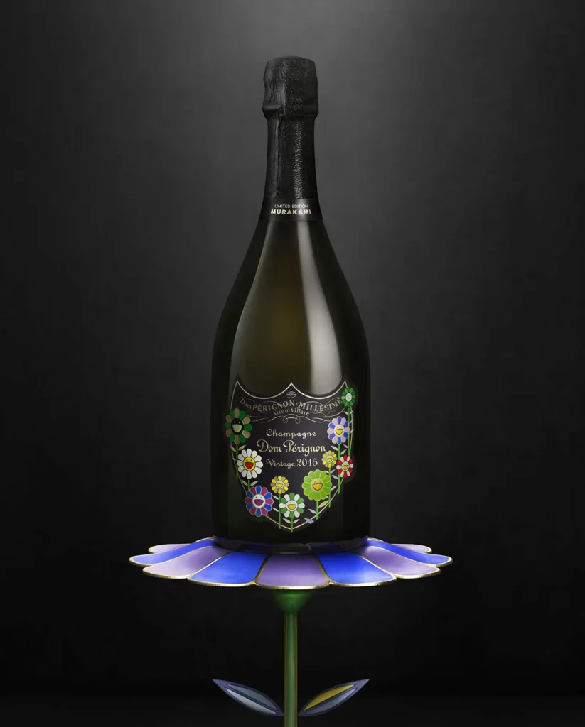 A Dom Pérignon Vintage 2015 champagne bottle from the Takashi Murakami limited edition is elegantly displayed atop a sculptural flower pedestal inspired by Murakami’s signature art. The dark bottle features colorful smiling flower motifs on the label, glowing against the minimalist black background, symbolizing the blend of haute champagne craftsmanship and play contemporary art.