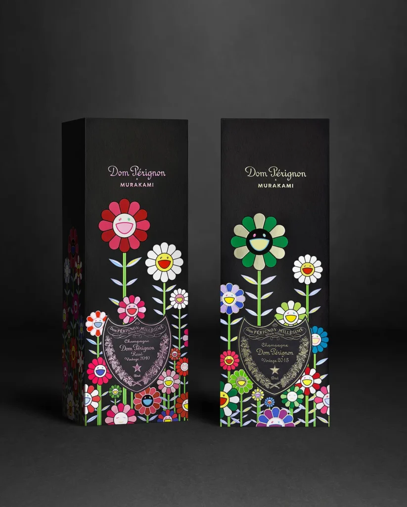 Two limited-edition Dom Pérignon x Takashi Murakami champagne boxes stand side by side against a dark background. The sleek black packaging is decorated with Murakami’s colorful smiling flower designs, representing the Rosé Vintage 2010 on the left and the Vintage 2015 on the right, uniting Dom Pérignon’s refined heritage with Murakami’s vibrant pop-art universe.