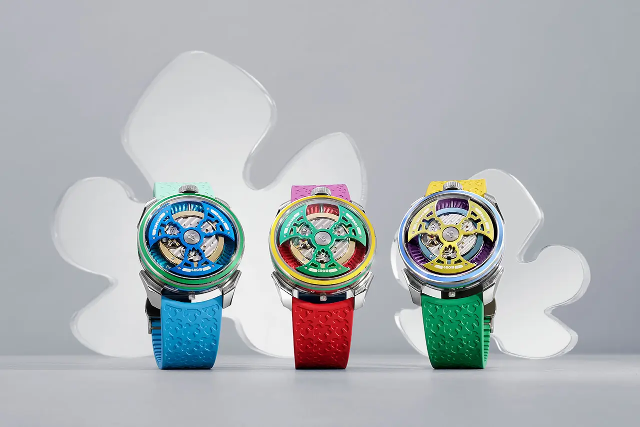 A trio of Yinka Ilori × MAD Editions × MB&F watches displayed upright against a soft grey backdrop, each featuring vibrant multicolored open-worked dials and textured rubber straps in blue, red, and green. The watches showcase Ilori’s signature joyful palette, with bold geometric accents and transparent mechanics visible beneath domed sapphire crystals