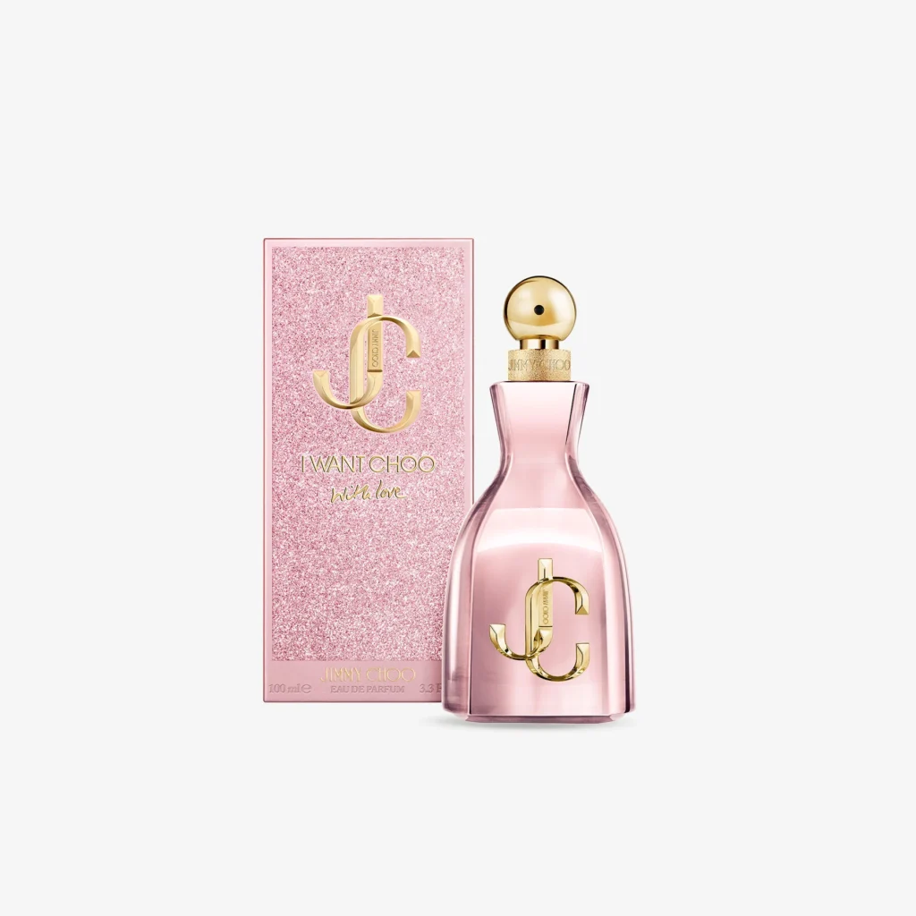 Jimmy Choo I Want Choo With Love perfume bottle and packaging — a sleek blush-pink glass bottle with gold “JC” monogram and matching spherical cap, placed beside a glittering rose box embossed with the same gold logo and “I Want Choo With Love” lettering, photographed on a light background