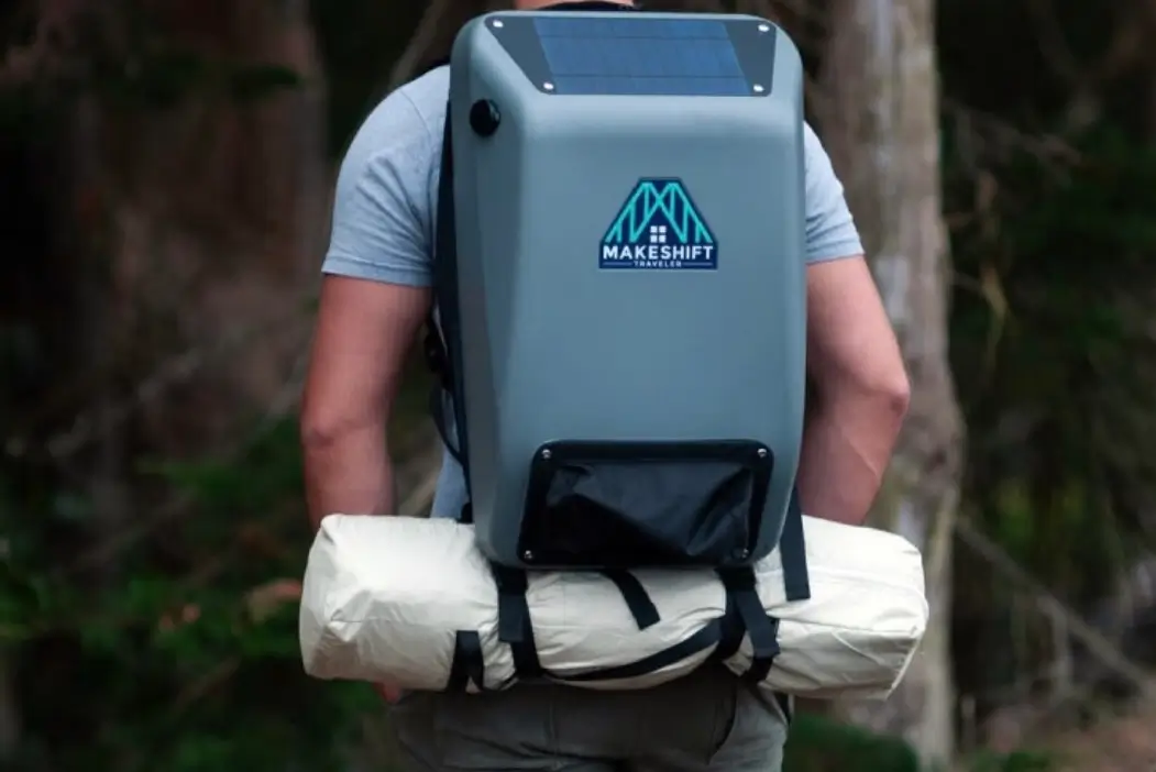 Person wearing the HomeMore Project’s Makeshift Traveler — a solar-powered backpack with a grey hardshell exterior, top-mounted solar panel, and attached rolled sleeping bag, designed to provide sustainable energy, storage, and comfort for individuals experiencing homelessness