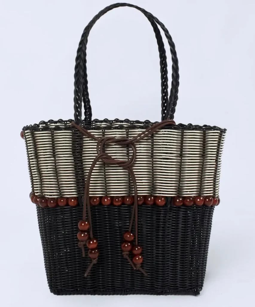 Wynn Hamlyn woven tote bag crafted from black and cream wicker, featuring braided handles, brown wooden bead trim, and a knotted leather cord tie accent, displayed against a light background