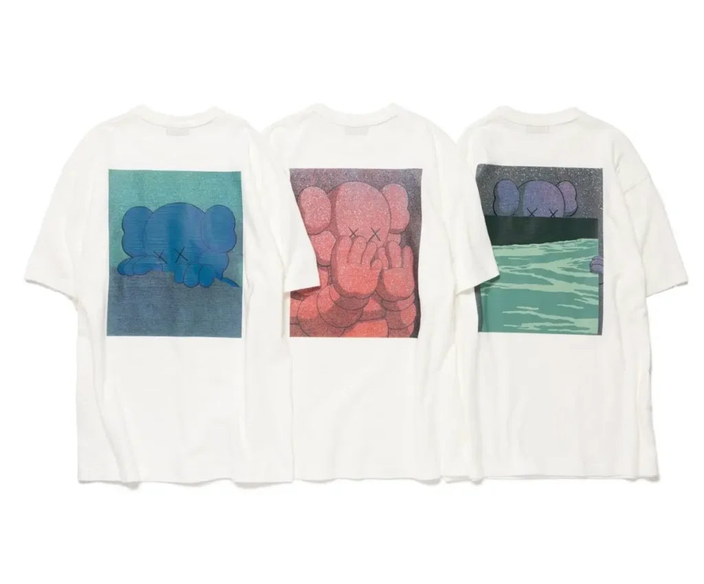 Three white HUMAN MADE × KAWS T-shirts from the 2025 “KAWS MADE” collection, featuring large back prints of KAWS’ Companion character in blue, red, and purple-green colorways, blending pop art emotion with NIGO®’s minimalist streetwear craftsmanship