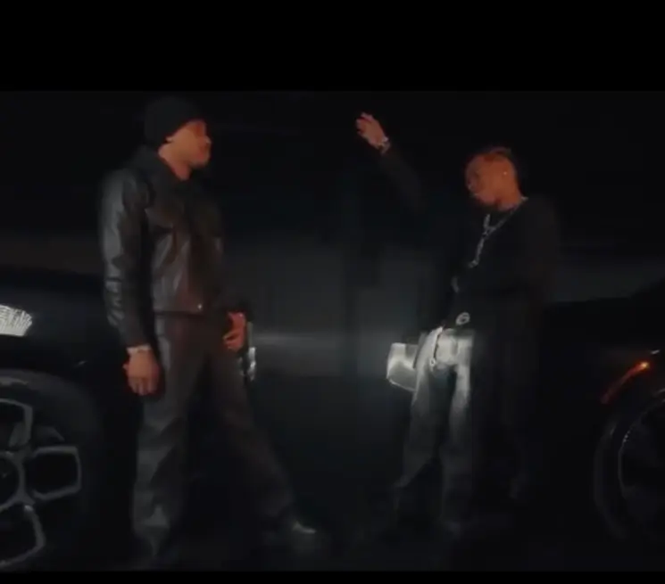 Lil Baby and G Herbo stand beside luxury black cars in a dimly lit scene, dressed in dark leather and chains, evoking a cinematic mood of triumph and tension from the All On Me music video