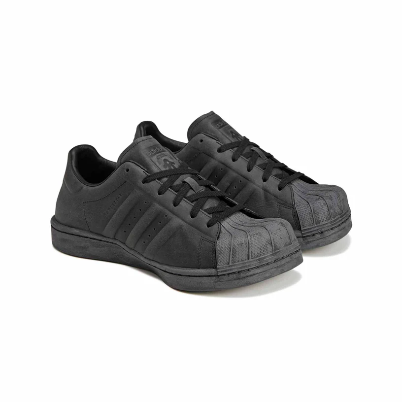 A pair of all-black Adidas by AVAVAV Women’s Superstar shoes featuring distorted paneling, an exaggerated shell toe, matte leather uppers, and AVAVAV’s signature misaligned detailing, photographed in a three-quarter front angle on a white background