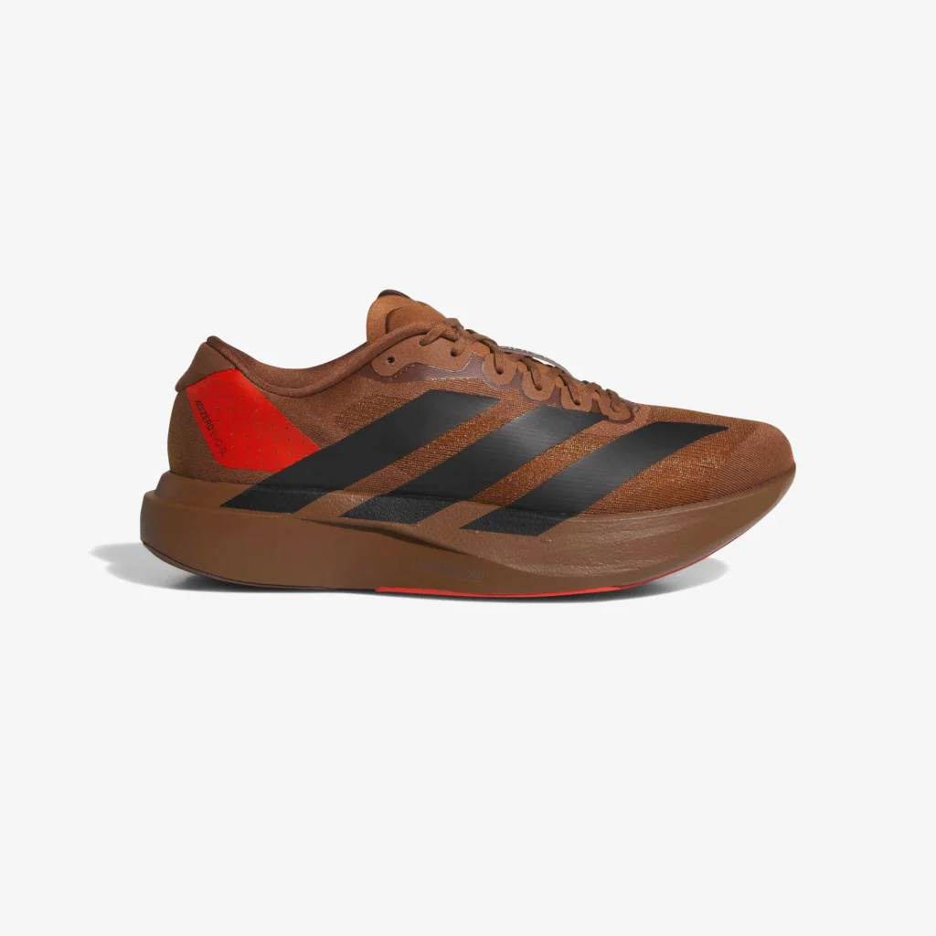 Side profile of the Pharrell Williams x adidas Adizero EVO SL “Preloved Brown” sneaker showcasing its rich brown mesh upper, bold black three-stripes, and contrasting red heel accent on a clean white background, emphasizing the shoe’s sleek, aerodynamic design and earthy palette