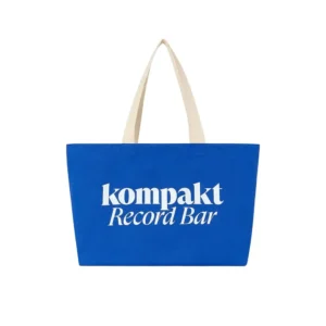 Blue Kompakt Record Bar canvas tote bag featuring large white ‘kompakt Record Bar’ text on the front and cream-colored handles, photographed against a white background