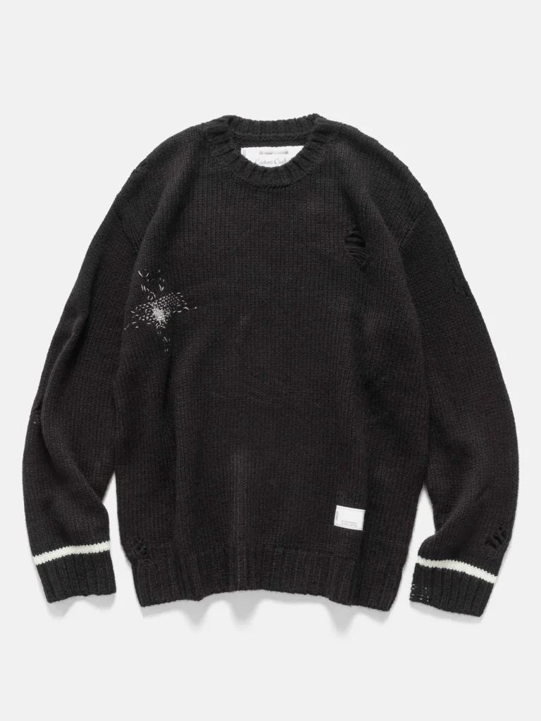 Front view of a black NEIGHBORHOOD Savage Crewneck Sweater featuring intentional distressing on the chest, shoulder, and sleeves, ribbed collar and hem, white stripe detailing on the cuffs, and a small woven label near the lower hem, laid flat on a light background