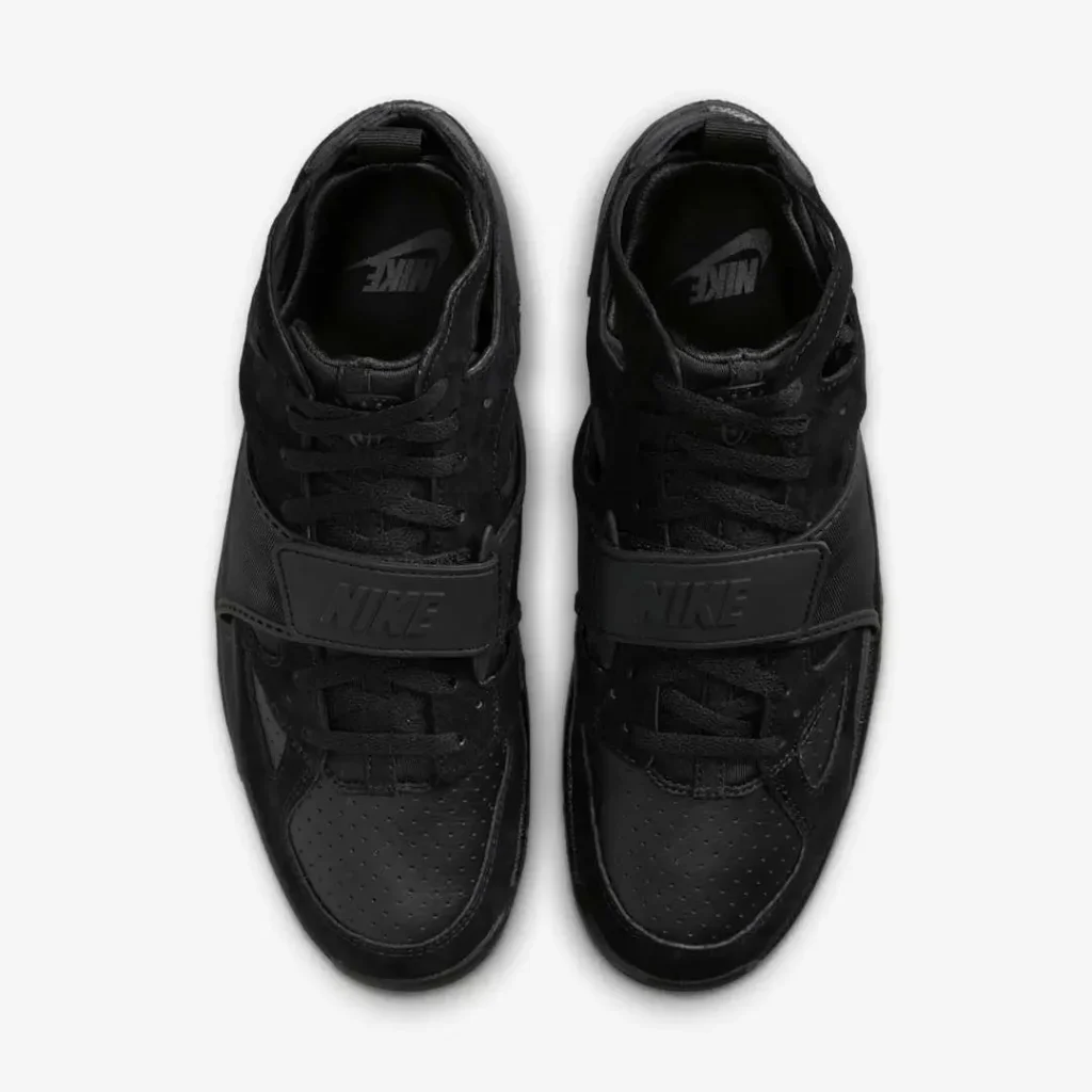 Top-down view of the Nike Air Trainer Huarache “Triple Black” sneakers, showing the symmetrical design with perforated leather toe boxes, tonal laces, and midfoot straps featuring embossed Nike logos, emphasizing the shoe’s sleek monochrome construction