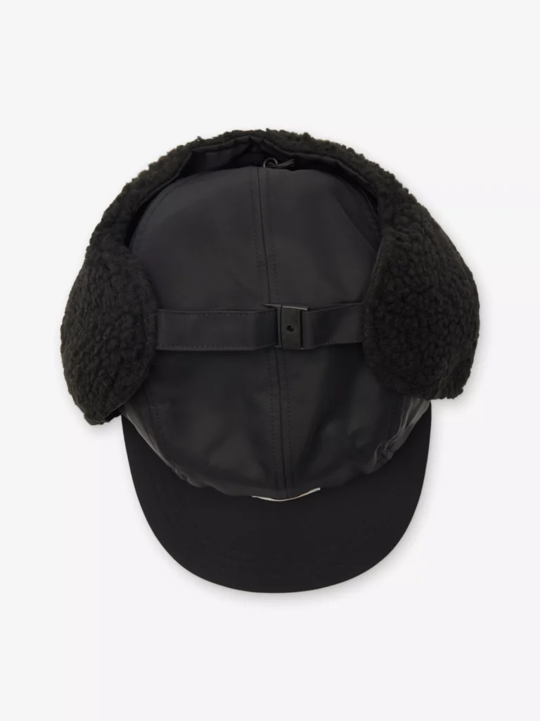 Top view of the Carhartt WIP Oltera Ear-Flap Woven Cap in black, displaying the fleece-lined ear flaps, stitched panels, and adjustable strap detail across the crown