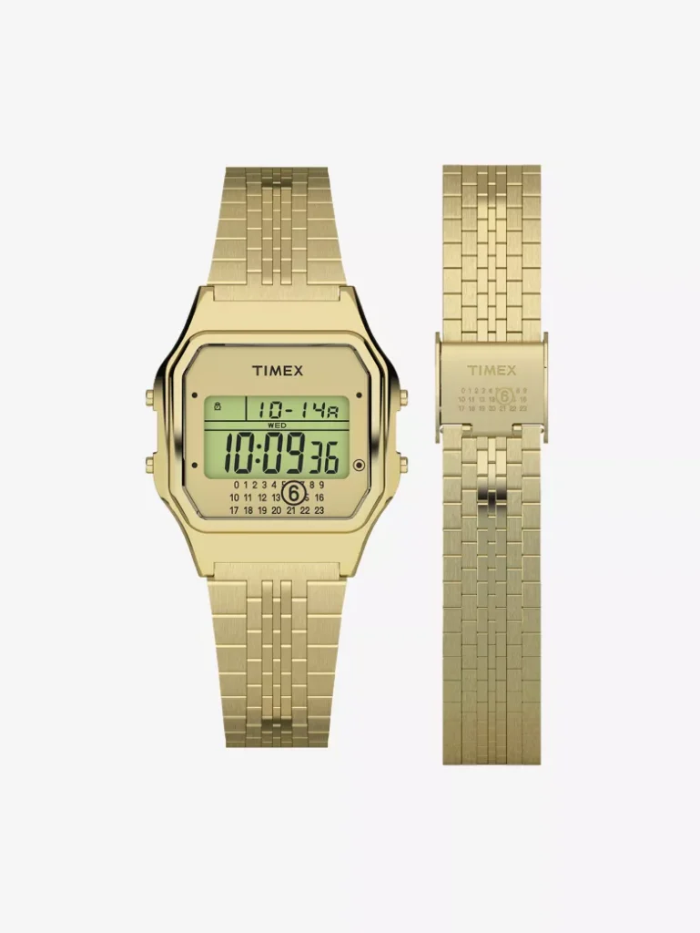 Front view of the Timex x MM6 Maison Margiela T80 gold-tone stainless-steel digital watch alongside its matching extra bracelet, showing the mirrored dial with MM6’s circled number 6 and the woven metal link design