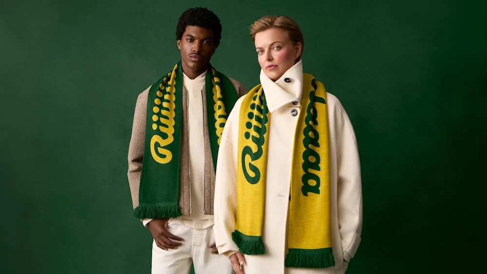 Two models wear Ricola’s herbal-scented winter scarves in green and yellow, styled against a deep green backdrop. The scarves feature bold Ricola branding and are paired with neutral, layered outerwear