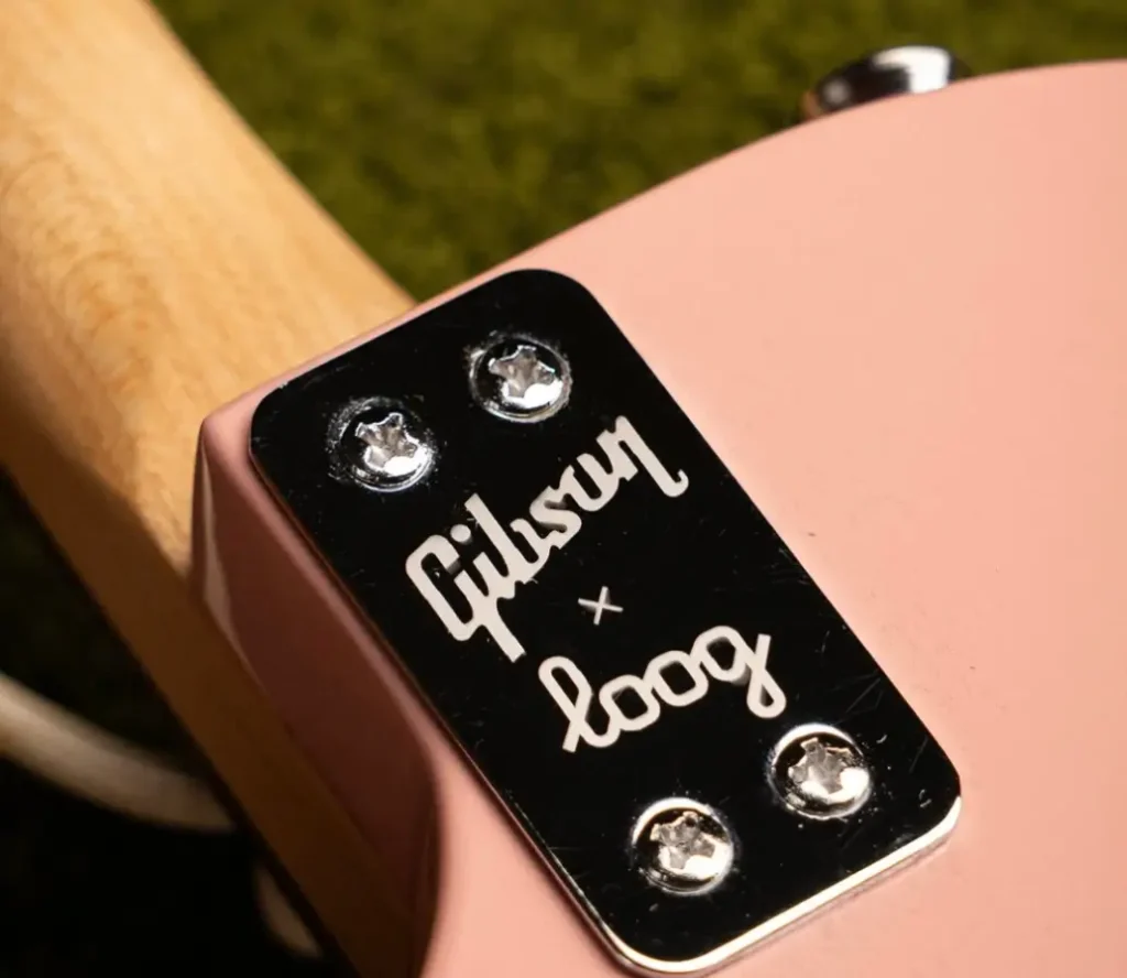 lineup of four Gibson x Loog electric guitars standing upright on green carpet against a white wall, featuring pastel blue, cherry red, TV yellow, and blush pink finishes, each with three strings and black pickguards, showcasing the playful yet classic mini Les Paul and SG-inspired designs