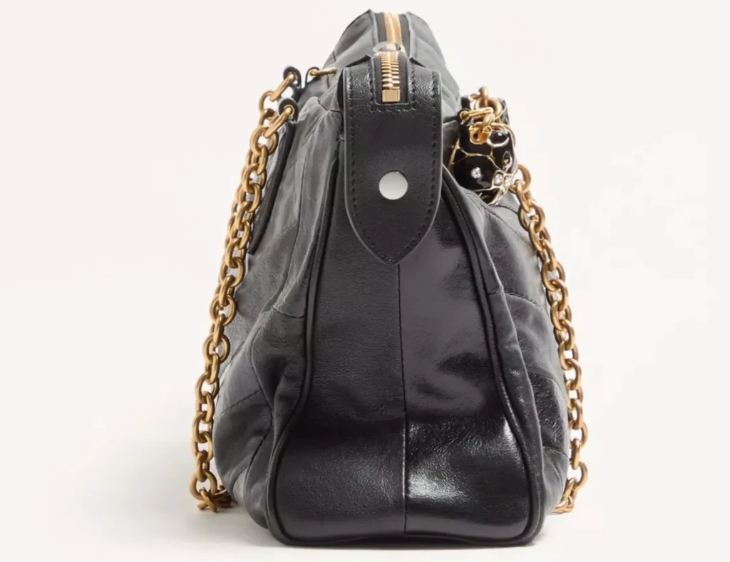 Side profile of the Valentino Garavani Panthea Shoulder Bag in black nappa leather with chevron stitching. The image highlights the bag’s structured silhouette, antique gold-tone chain strap, polished leather side panels, and zipper closure along the top, emphasizing its refined craftsmanship and sculptural form