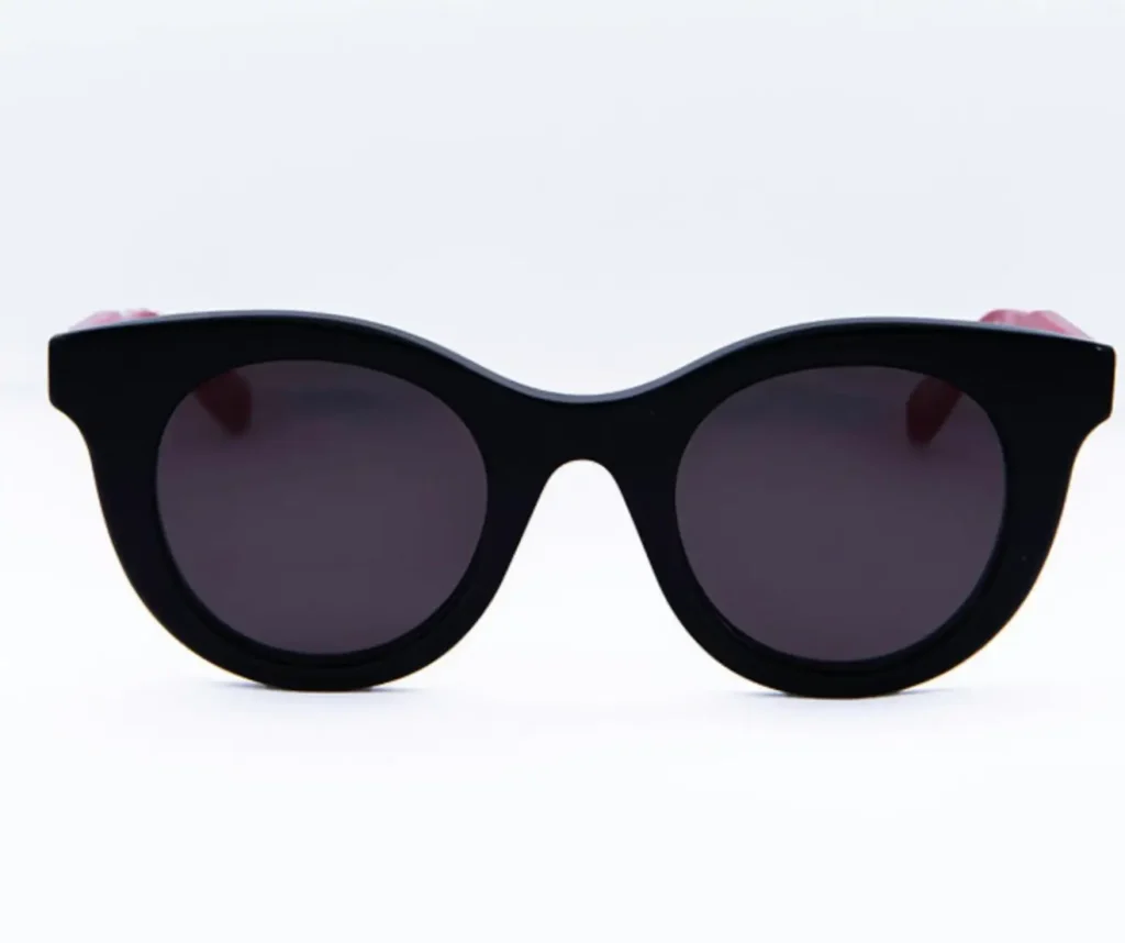 Black oval-shaped sunglasses with a thick, glossy acetate frame and dark tinted lenses, photographed from the front against a clean white background