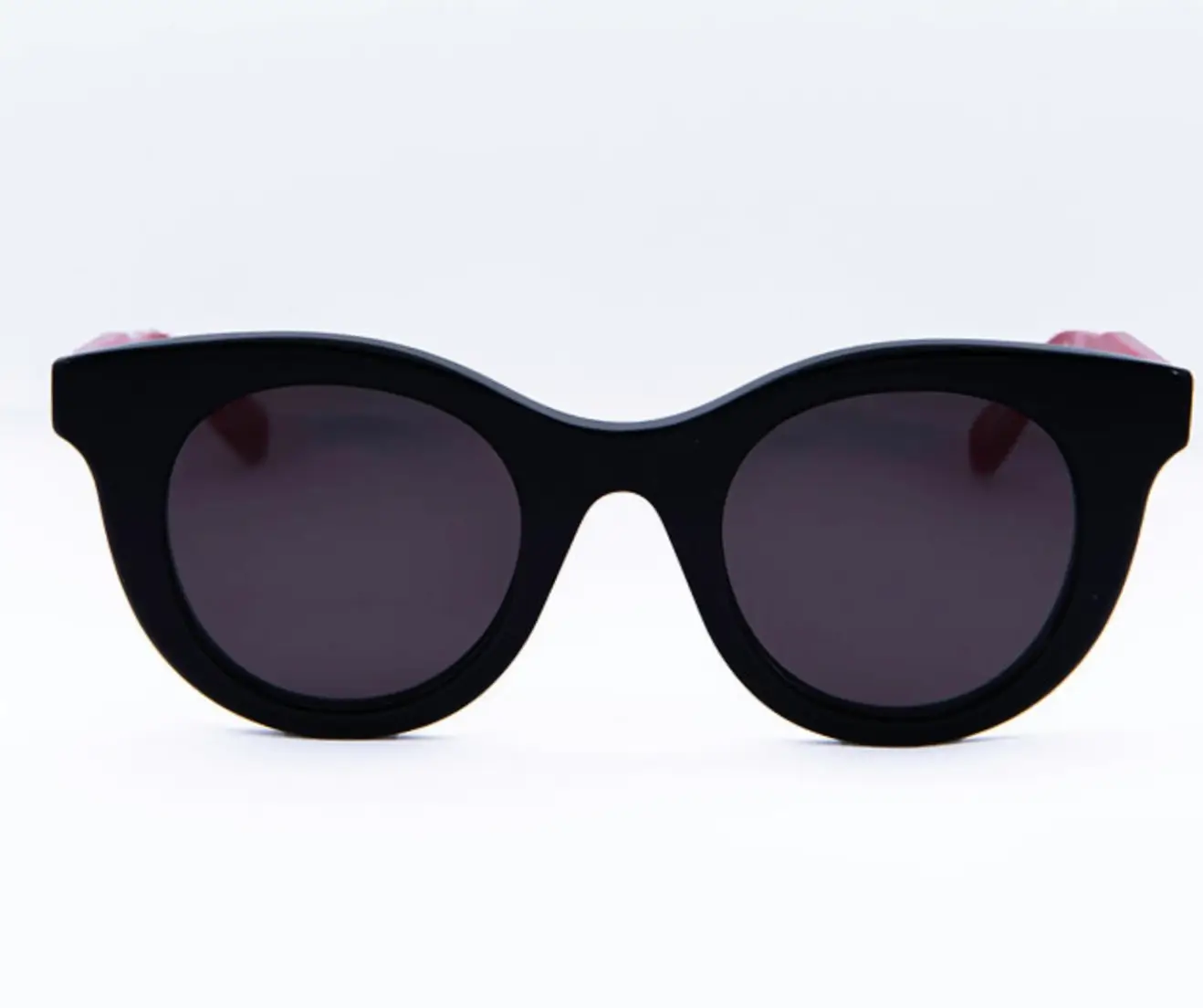 Black oval-shaped sunglasses with a thick, glossy acetate frame and dark tinted lenses, photographed from the front against a clean white background