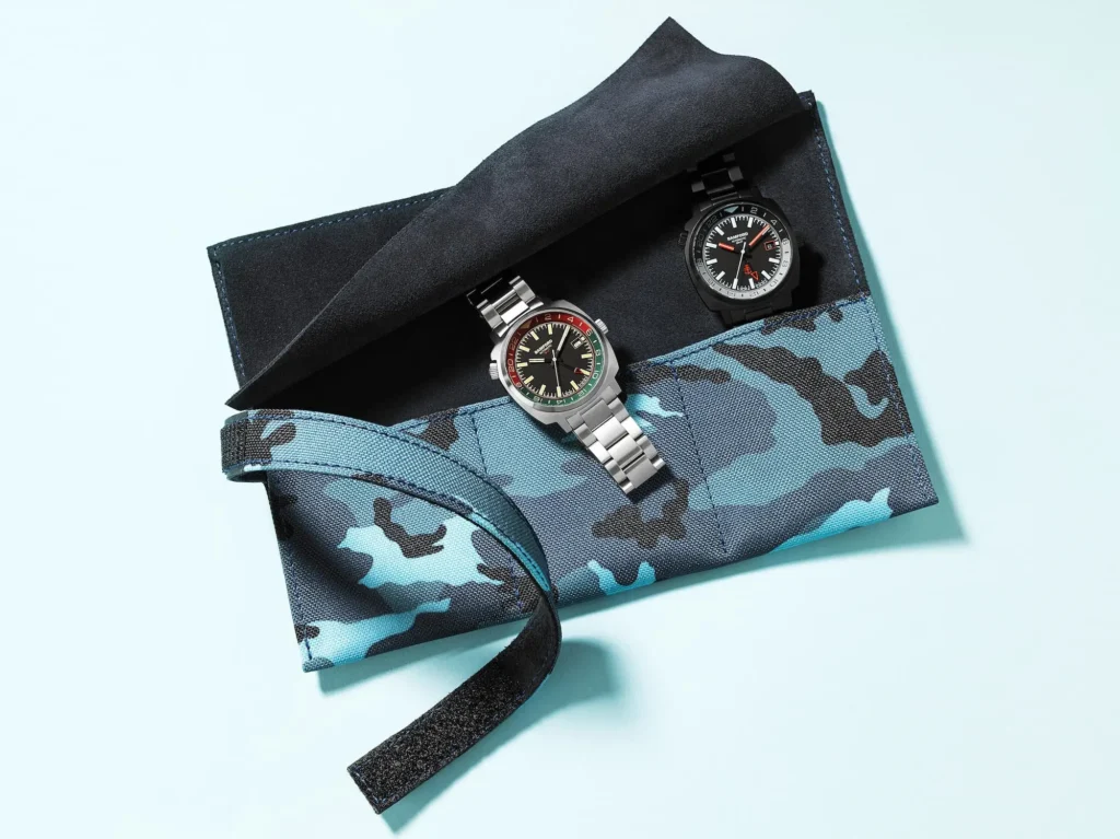 Aqua blue and petrol black camouflage three-pocket watch roll made of Cordura canvas, opened to reveal two wristwatches resting inside a soft black suede interior, displayed on a light blue background